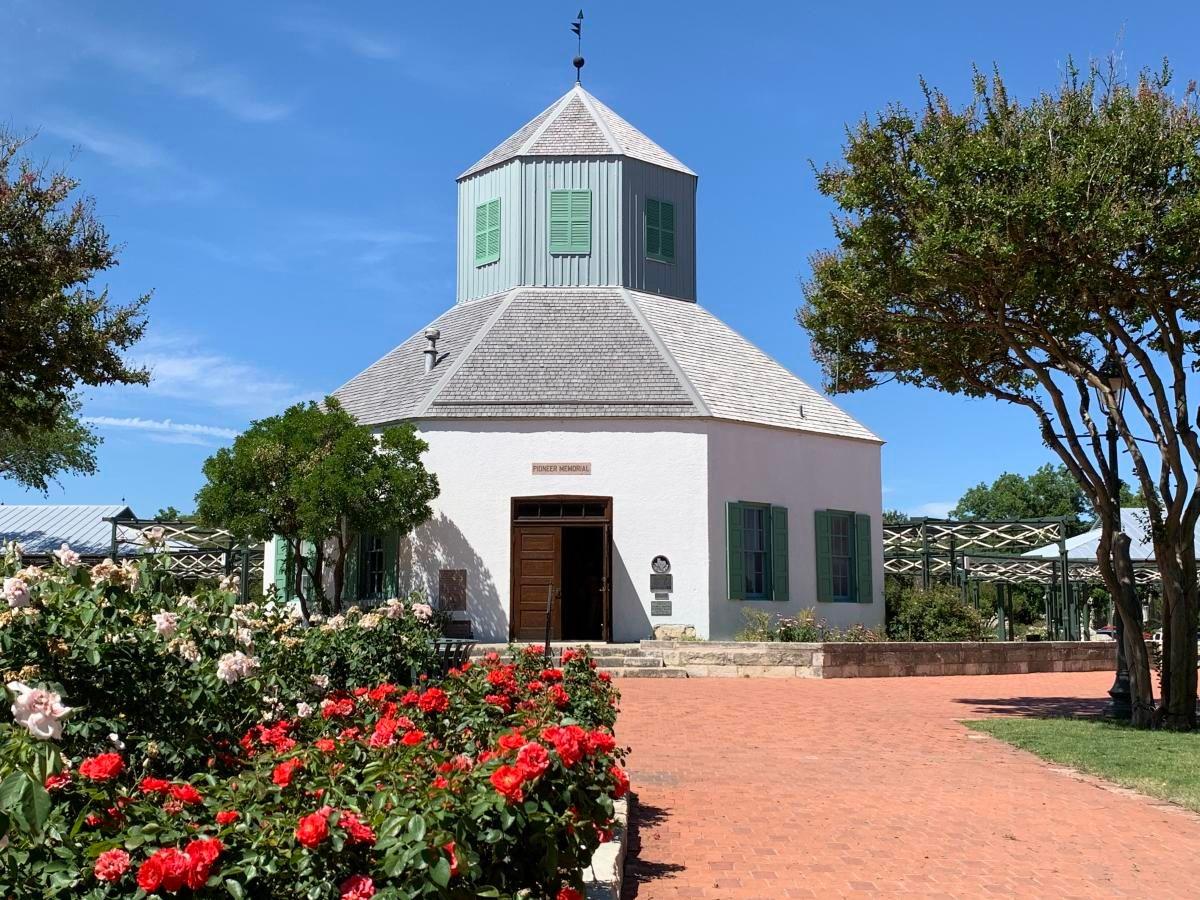 Historic octagonal building with garden and red flowers under a blue sky.